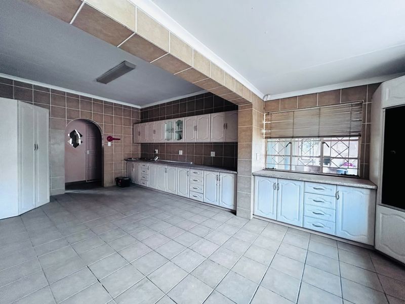 Spacious kitchen featuring extensive built-in cabinetry, tiled walls and flooring, and a distinct architectural archway, offering a blank canvas for modern renovation.