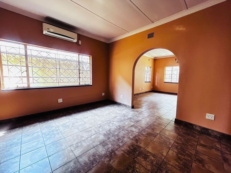 An empty living area featuring tiled flooring, an arched transition to an adjacent room, and a wall-mounted air conditioning unit.
