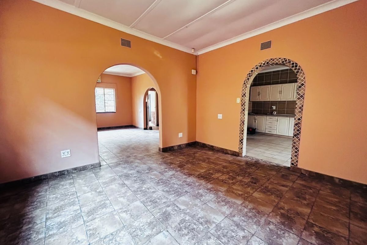 An empty living area featuring tiled floors, arched doorways with decorative trim, and neutral wall finishes, providing a versatile space for renovation.