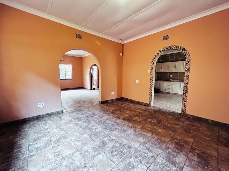 An empty living area featuring tiled floors, arched doorways with decorative trim, and neutral wall finishes, providing a versatile space for renovation.