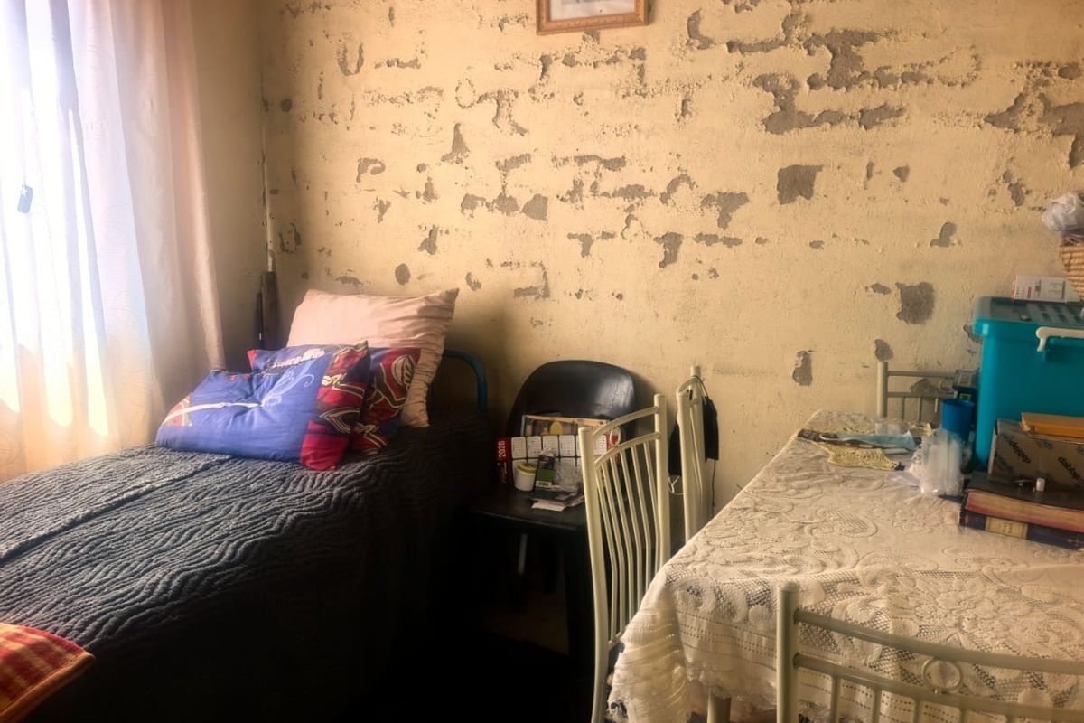 A bedroom featuring a window and walls requiring significant plaster repair and repainting to restore the interior finish.