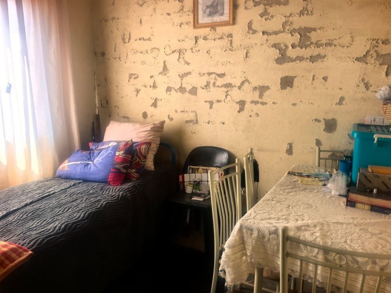 A bedroom featuring a window and walls requiring significant plaster repair and repainting to restore the interior finish.