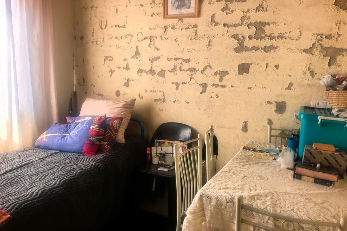 A bedroom featuring significant wall surface deterioration with extensive plaster damage and peeling paint, requiring substantial renovation and repair.
