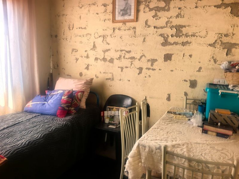 A bedroom featuring significant wall surface deterioration with extensive plaster damage and peeling paint, requiring substantial renovation and repair.
