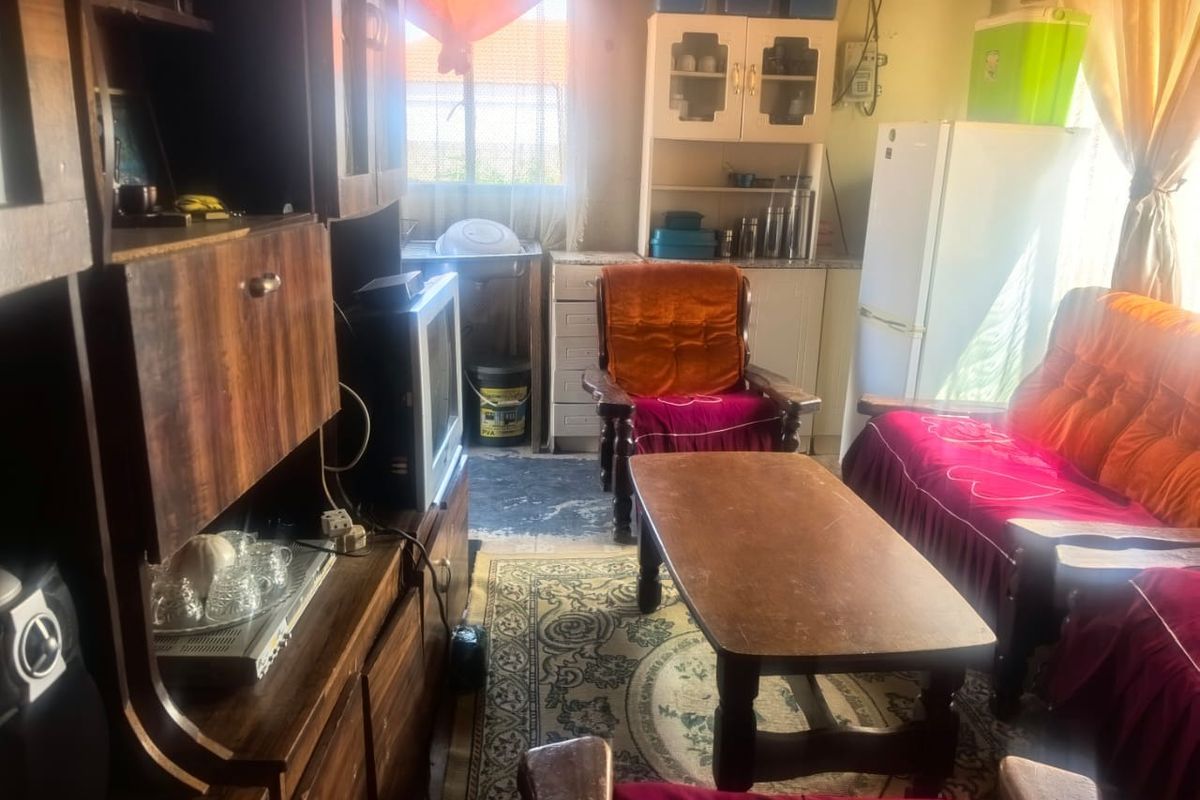 An open-plan living and kitchen area featuring dated built-in cabinetry and a functional sink, requiring cosmetic updates to modernize the space.