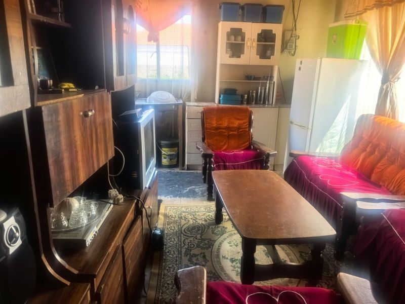 An open-plan living and kitchen area featuring dated built-in cabinetry and a functional sink, requiring cosmetic updates to modernize the space.
