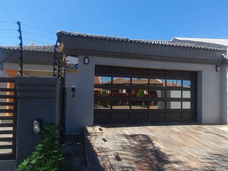 Front exterior view featuring a modern automated garage door, tiled driveway, and secure perimeter wall with electric fencing.