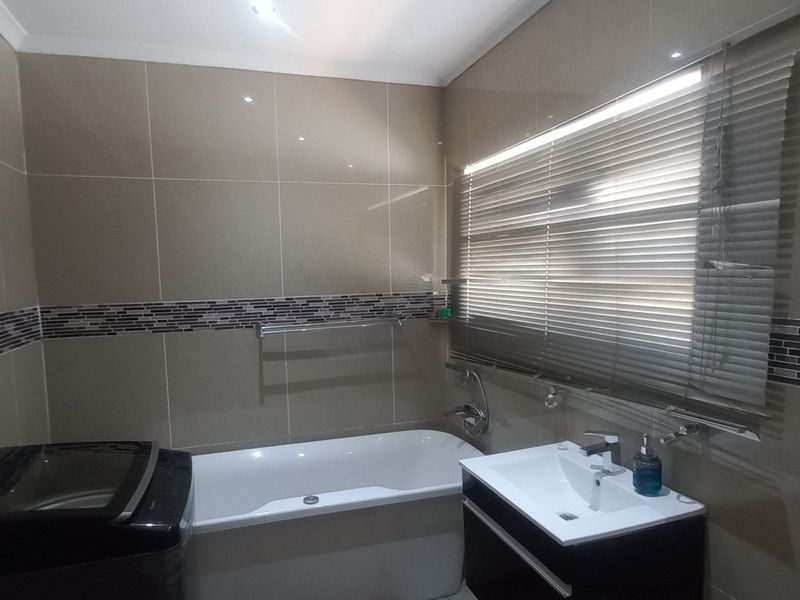 A modern bathroom featuring tiled walls, a built-in bathtub, and a sleek vanity cabinet with a basin.
