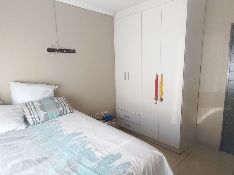 A functional bedroom featuring neutral wall tones, tiled flooring, and a white built-in wardrobe providing ample storage space.