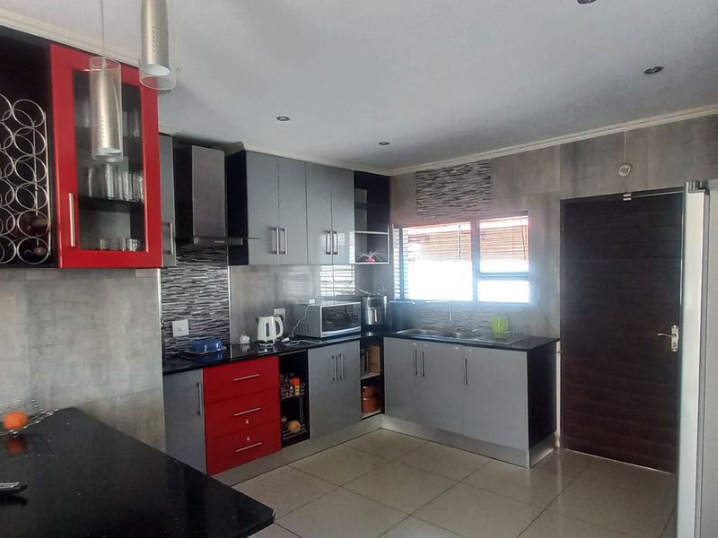 Modern kitchen featuring contrasting red and grey cabinetry, granite countertops, integrated extractor fan, and tiled flooring with direct access to an exterior door.
