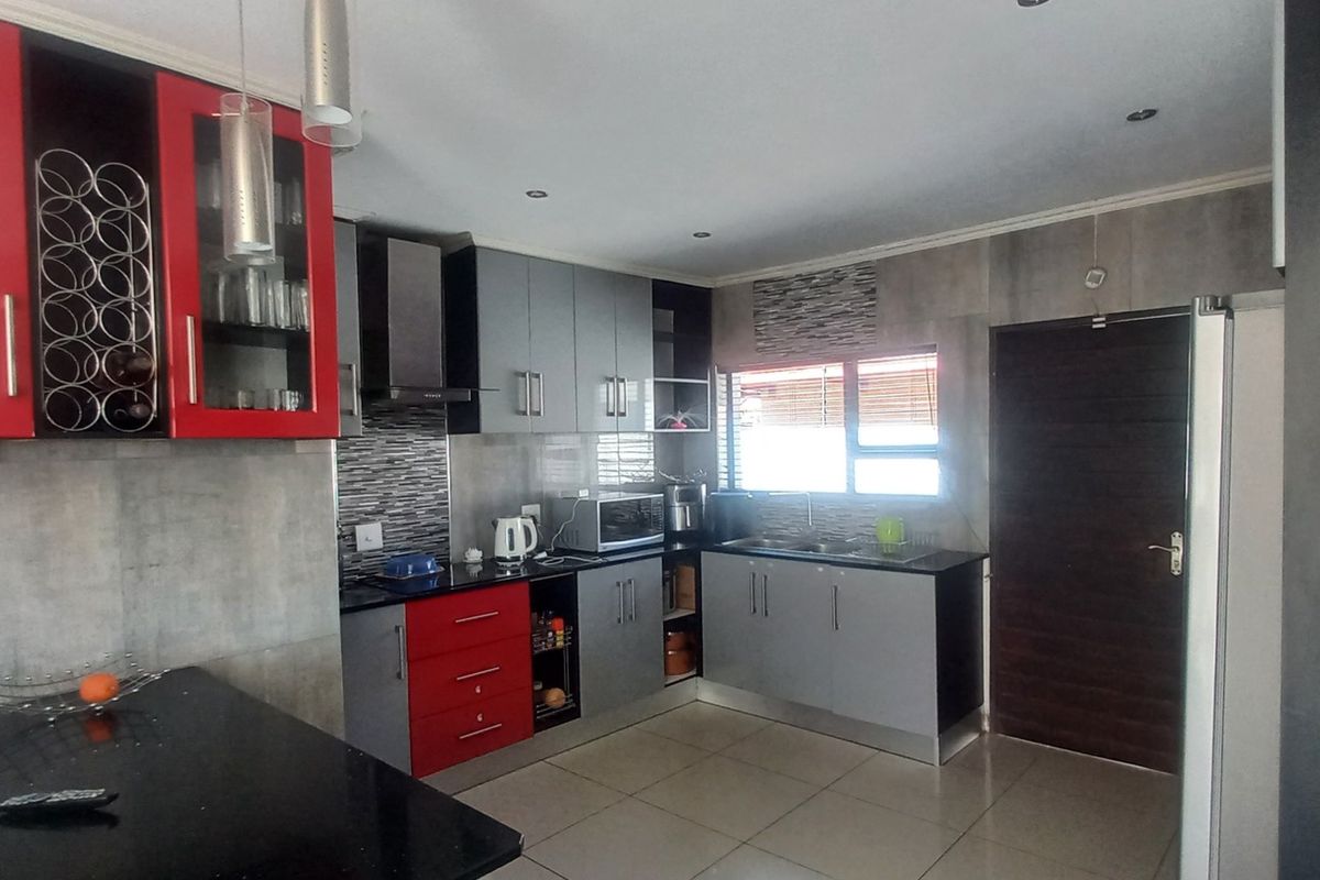 Modern kitchen featuring contrasting red and grey cabinetry, granite countertops, integrated extractor fan, and tiled flooring with direct access to an exterior door.