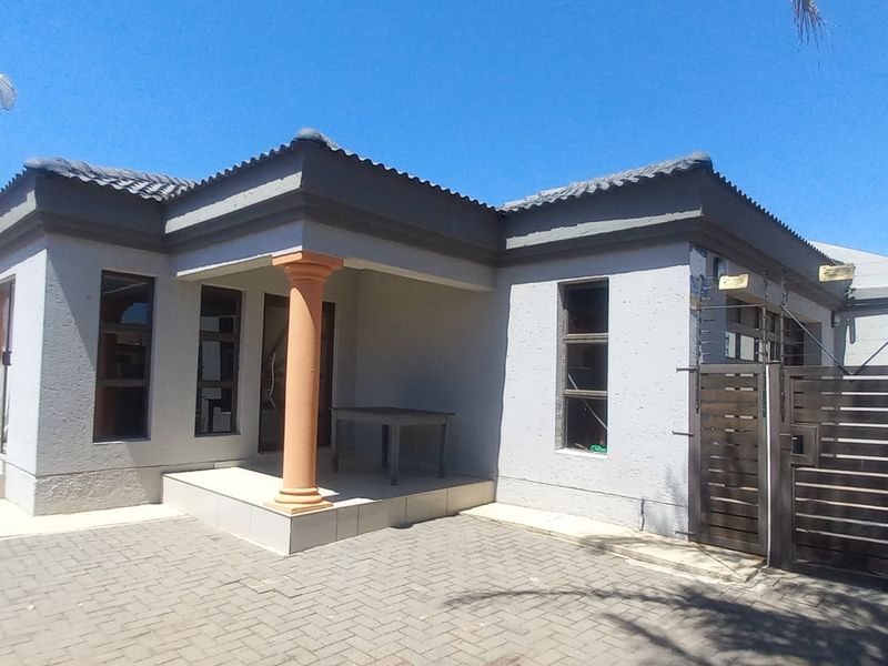 Front view of a single-story house featuring a paved driveway, covered entrance porch with a decorative column, and secure perimeter electric fencing.