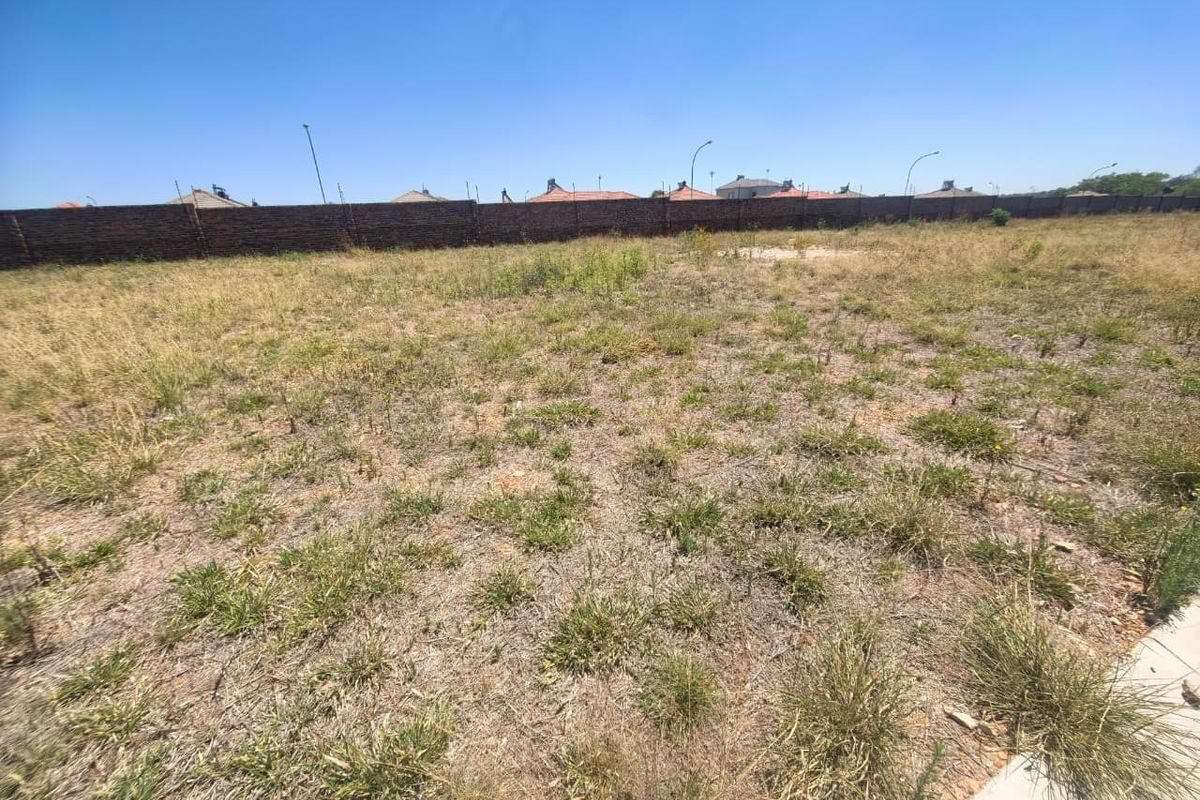 A vacant residential plot featuring natural grass coverage and a perimeter brick boundary wall.