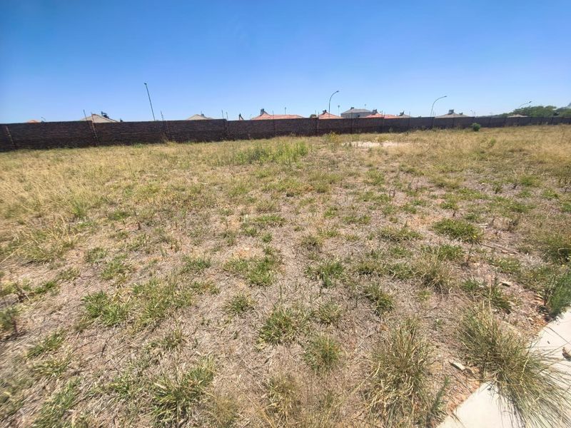 A vacant residential plot featuring natural grass coverage and a perimeter brick boundary wall.