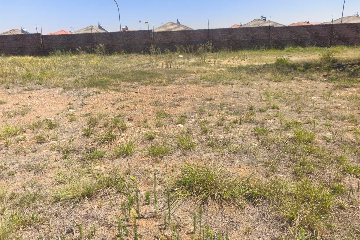 A vacant residential plot featuring natural grass cover, enclosed by a perimeter brick wall with installed electric fencing.