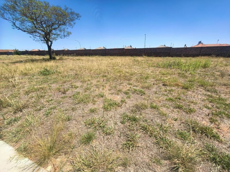 A vacant residential plot featuring natural grass cover, a mature tree, and a secure perimeter brick wall boundary.