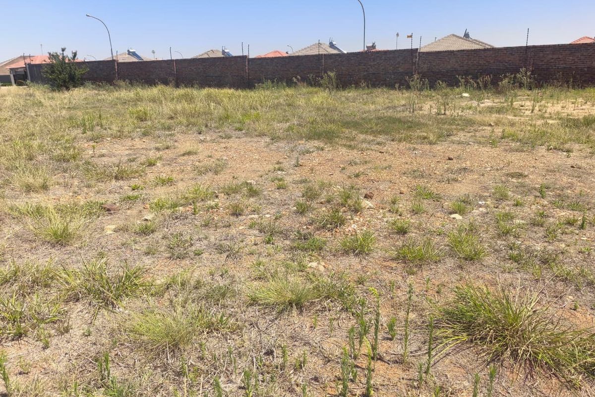 A vacant residential plot featuring natural grass coverage, enclosed by a brick perimeter wall with installed electric fencing.