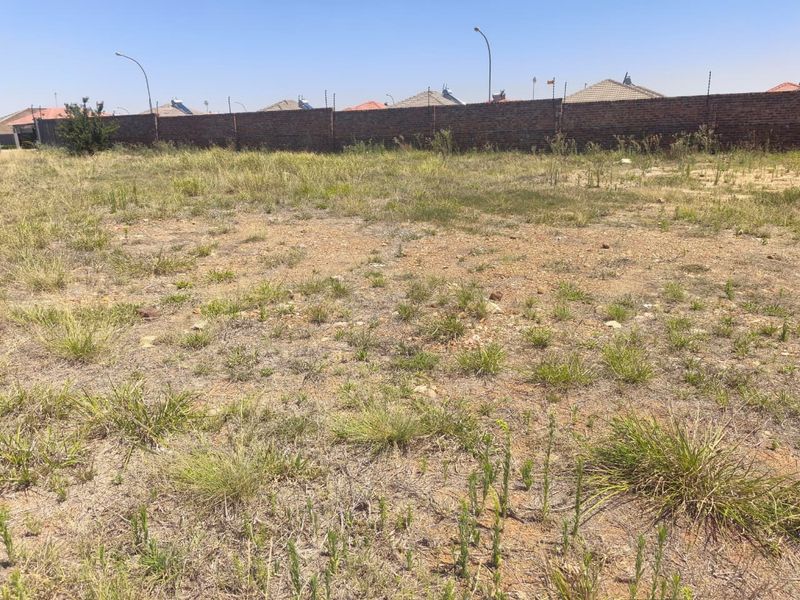 A vacant residential plot featuring natural grass coverage, enclosed by a brick perimeter wall with installed electric fencing.