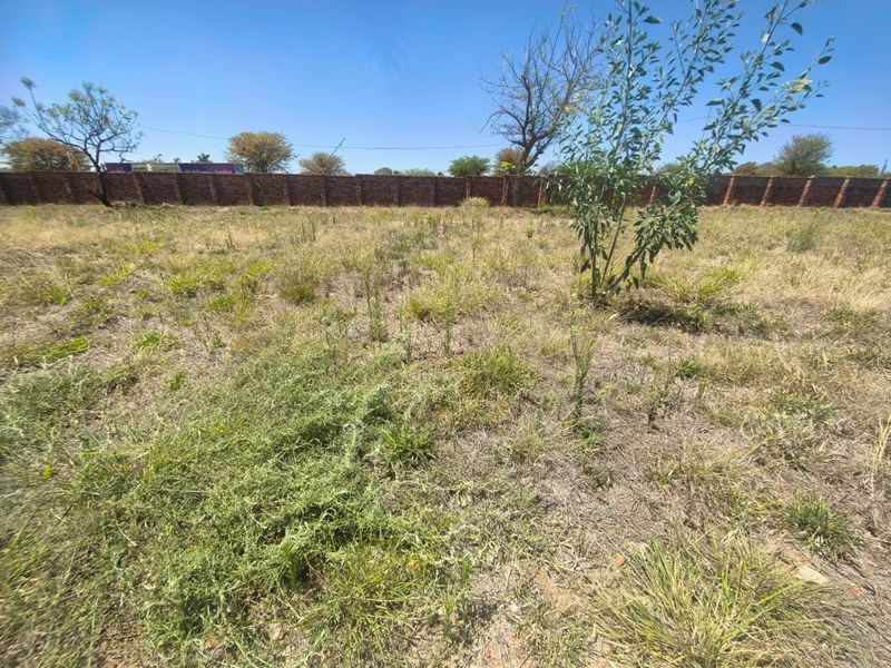 A vacant residential plot featuring natural grass coverage and a secure perimeter brick wall boundary.
