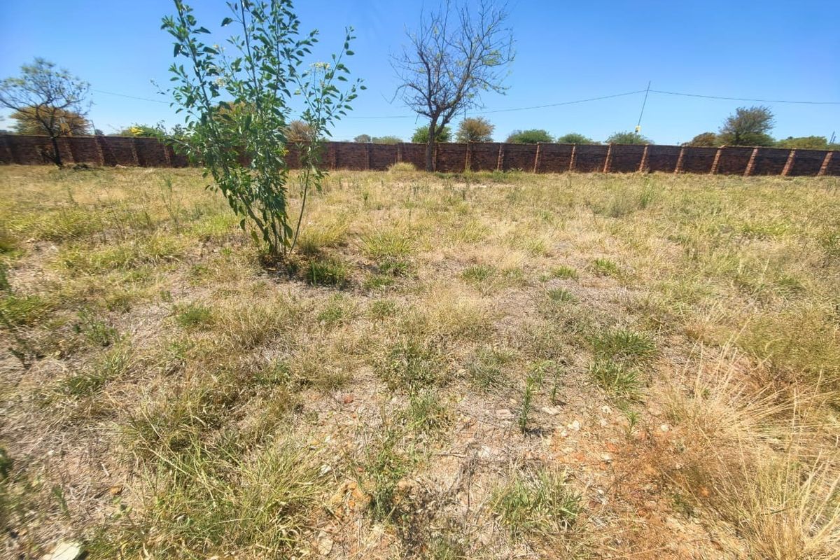 A vacant residential plot featuring natural grass coverage and a perimeter brick boundary wall.
