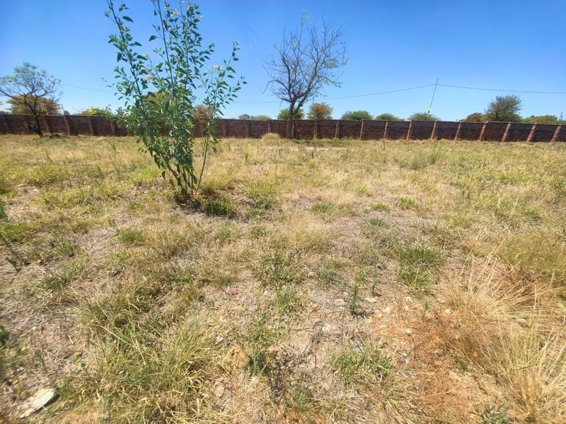 A vacant residential plot featuring natural grass coverage and a perimeter brick boundary wall.