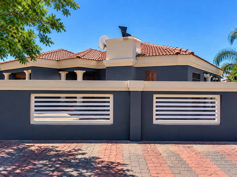 Front elevation of a modern house featuring a dark grey perimeter wall with white slatted inserts, a tiled roof, and a paved driveway.