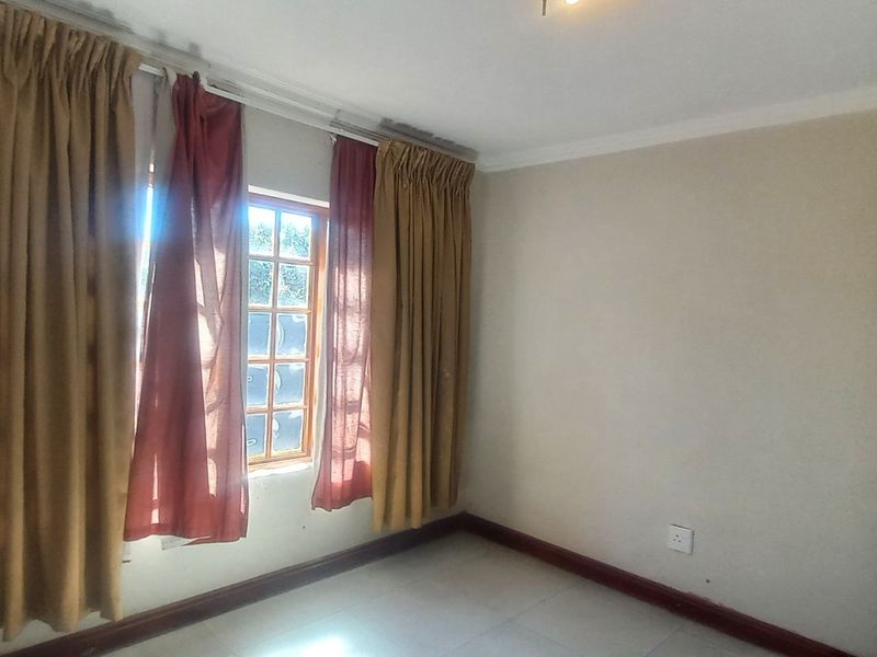 A vacant bedroom featuring tiled flooring, neutral walls, and a window with security bars, providing a clean and versatile space.