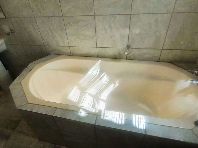 A functional bathroom featuring a built-in bathtub with tiled surround and a pedestal basin, finished with neutral wall and floor tiles.
