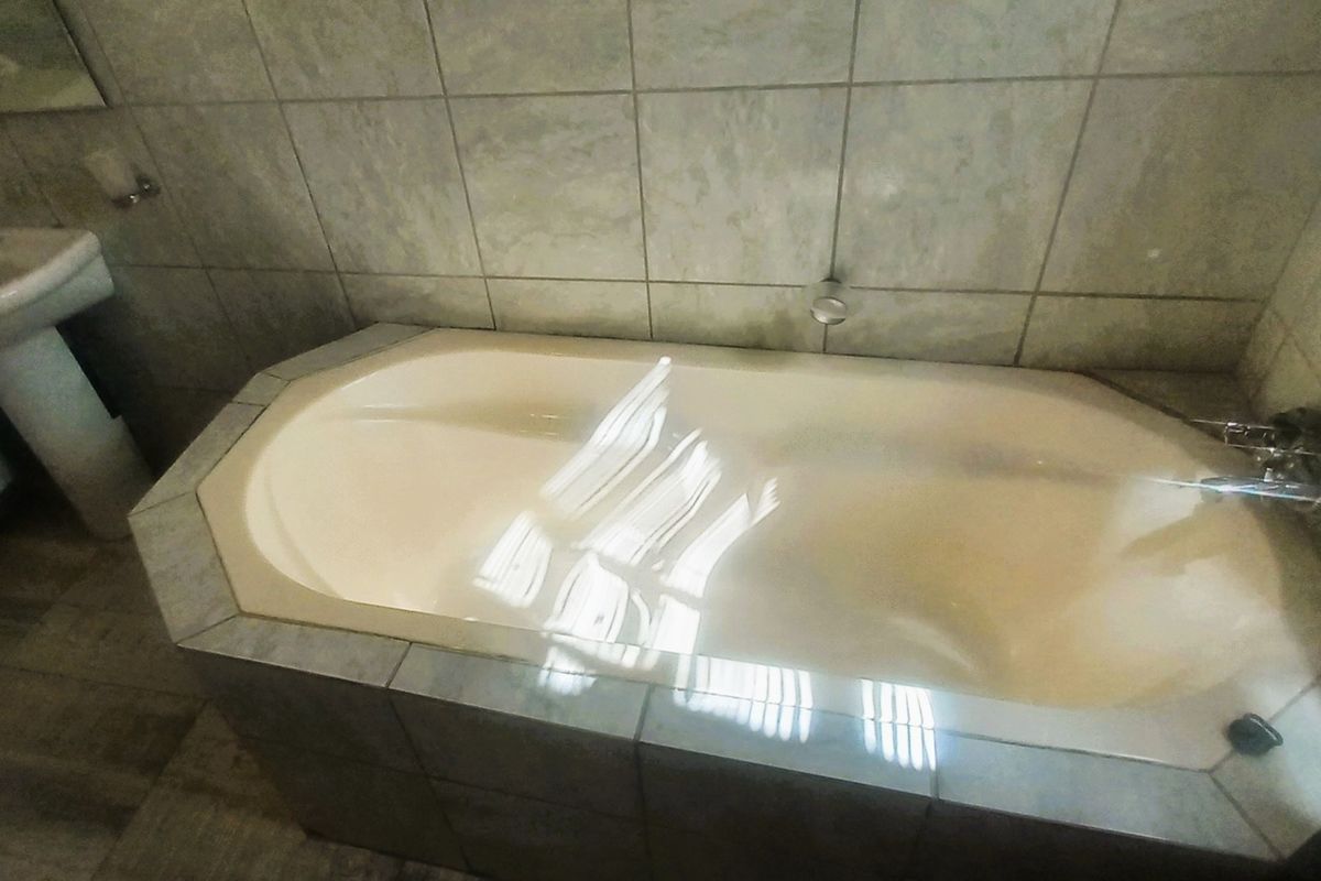 A functional bathroom featuring a built-in bathtub with tiled surround and a pedestal basin, finished with neutral wall and floor tiles.