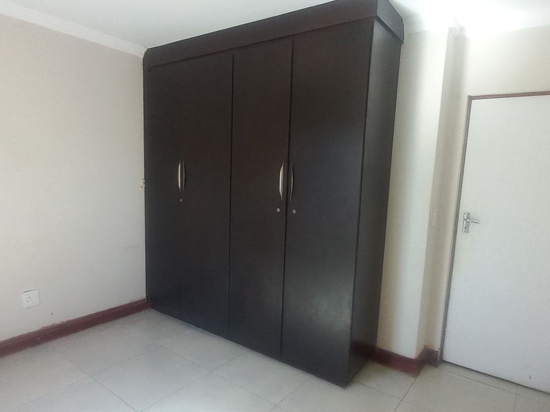 A clean, empty bedroom featuring neutral walls, tiled flooring, and a large dark wood built-in cupboard.