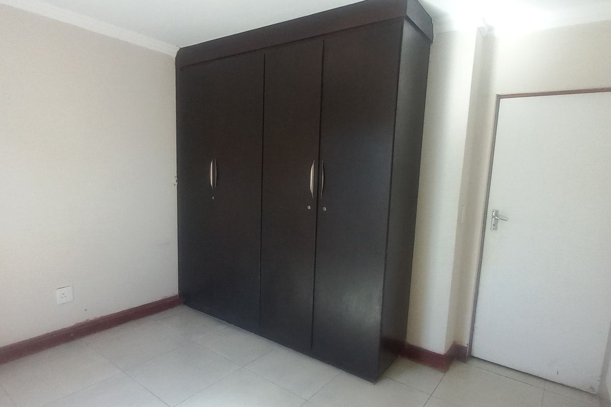 A clean, empty bedroom featuring neutral walls, tiled flooring, and a large dark wood built-in cupboard.