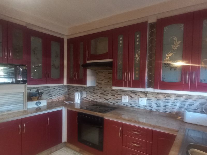 A functional kitchen featuring red cabinetry, mosaic tile backsplash, laminate countertops, and integrated appliances including an oven and hob.