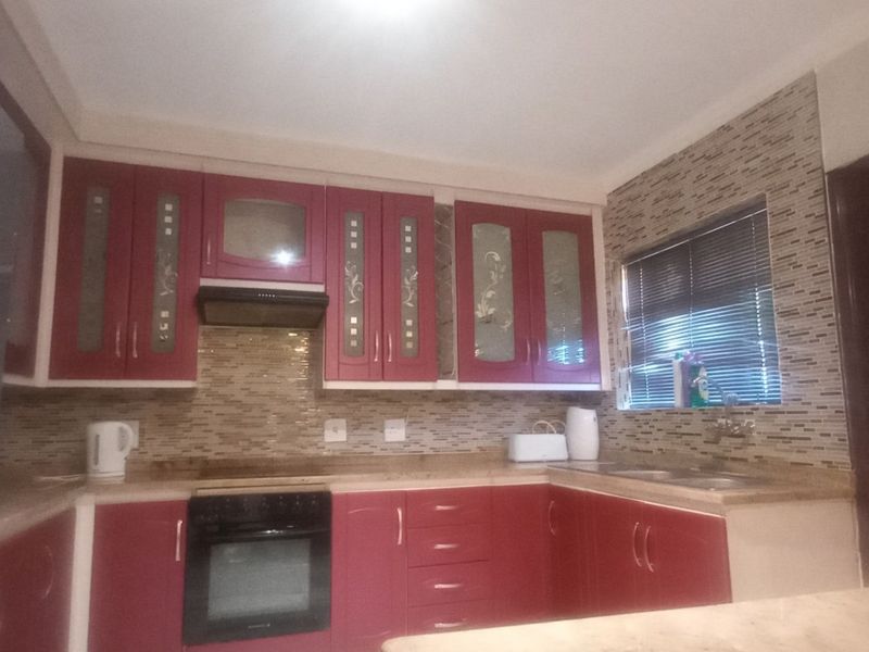 A kitchen featuring red cabinetry, mosaic tile backsplash, laminate countertops, and built-in oven with extractor fan.