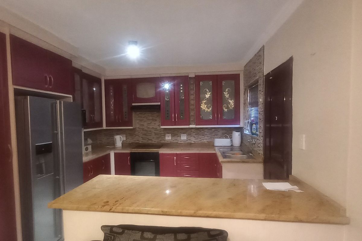 A functional kitchen featuring dark red cabinetry, granite countertops, a mosaic tile backsplash, and integrated appliances including an oven and hob.