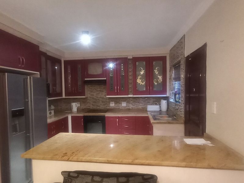 A functional kitchen featuring dark red cabinetry, granite countertops, a mosaic tile backsplash, and integrated appliances including an oven and hob.