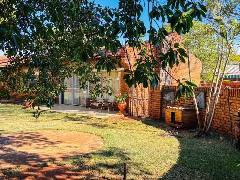 A rear view of the house featuring a brick facade, a paved patio area, and a well-maintained garden space.