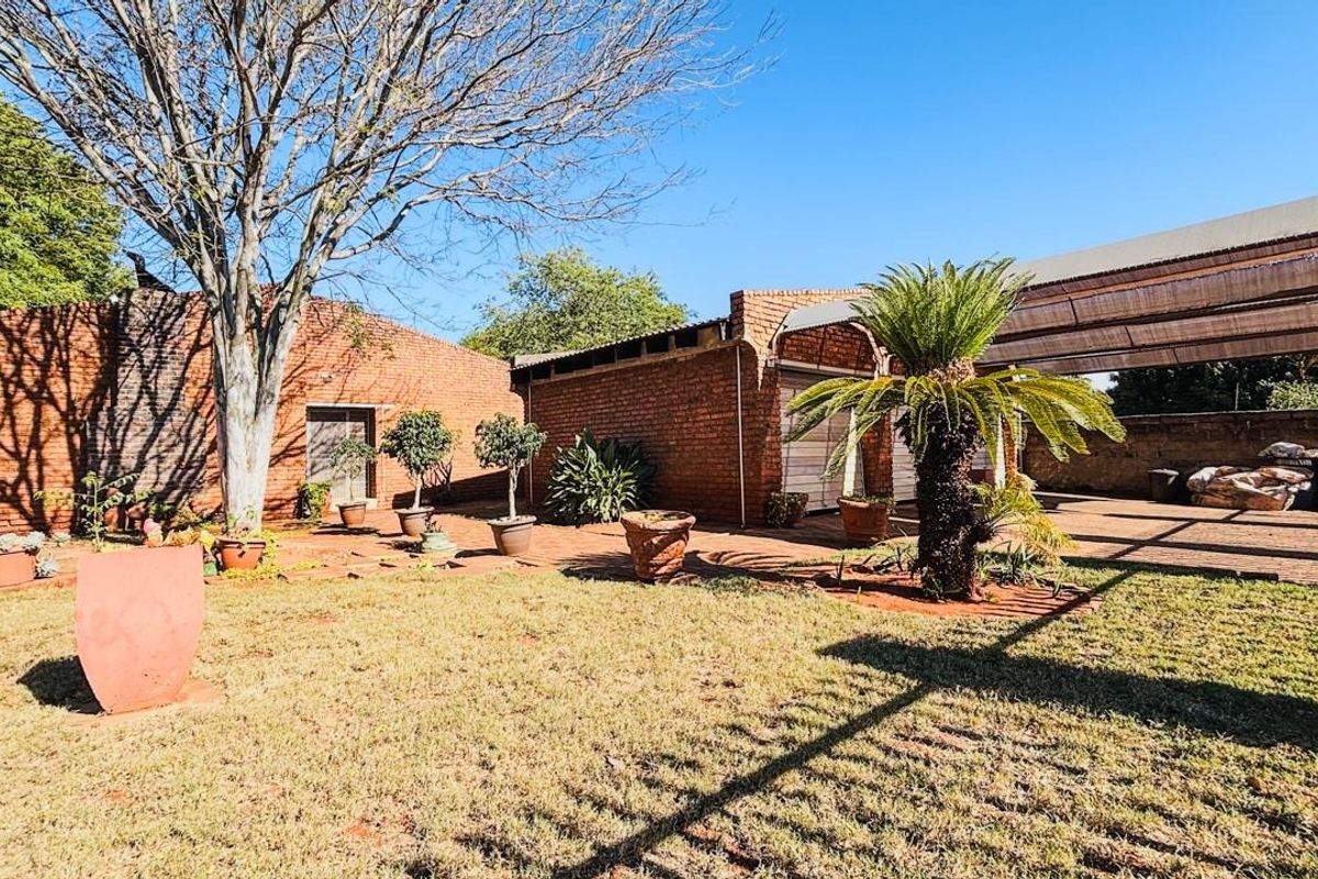 A spacious rear garden featuring an exposed brick facade, a paved courtyard area, and a covered patio space.