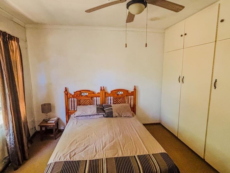 A bedroom featuring built-in cupboards, a ceiling fan, and an air conditioning unit, with carpeted flooring and neutral wall finishes.