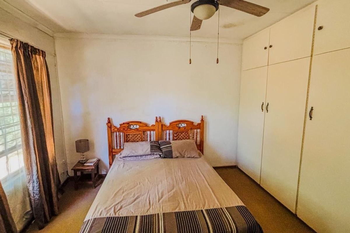 A bedroom featuring built-in cupboards, a ceiling fan, and an air conditioning unit, with carpeted flooring and neutral wall finishes.