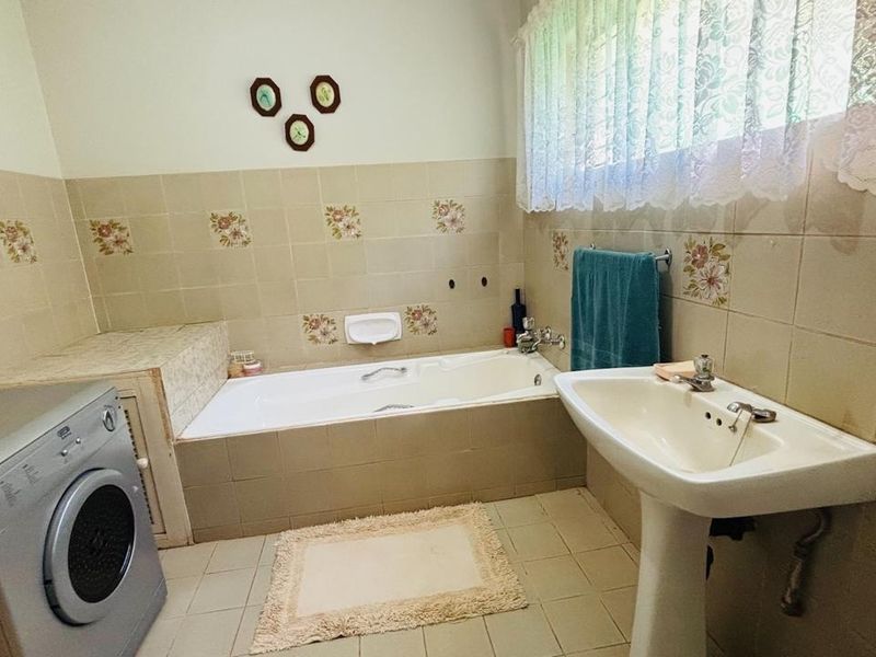 A dated bathroom featuring a built-in bathtub, pedestal washbasin, and neutral ceramic tiling throughout, offering potential for a modern renovation.