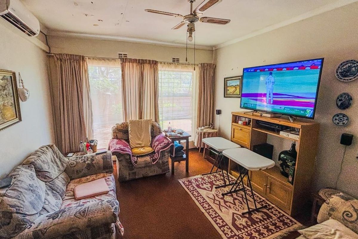 A living room featuring a ceiling fan, split-system air conditioning, and large windows. The ceiling shows signs of wear and water staining.