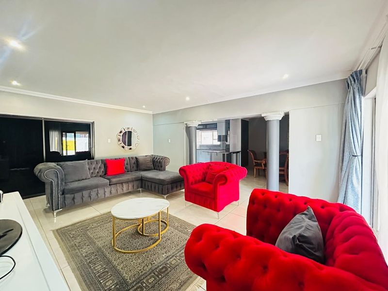 Spacious open-plan living area featuring tiled floors, decorative columns, and recessed lighting, with a seamless transition to the adjacent kitchen and dining space.
