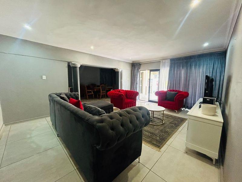 Spacious open-plan living area featuring large format floor tiles, decorative columns, and direct access to an outdoor space through sliding glass doors.