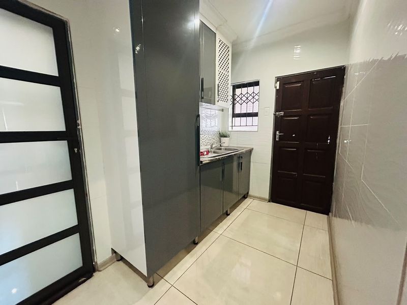 A clean and modern scullery area featuring sleek grey cabinetry, a stainless steel sink, and neutral tiled flooring with direct access to the exterior.