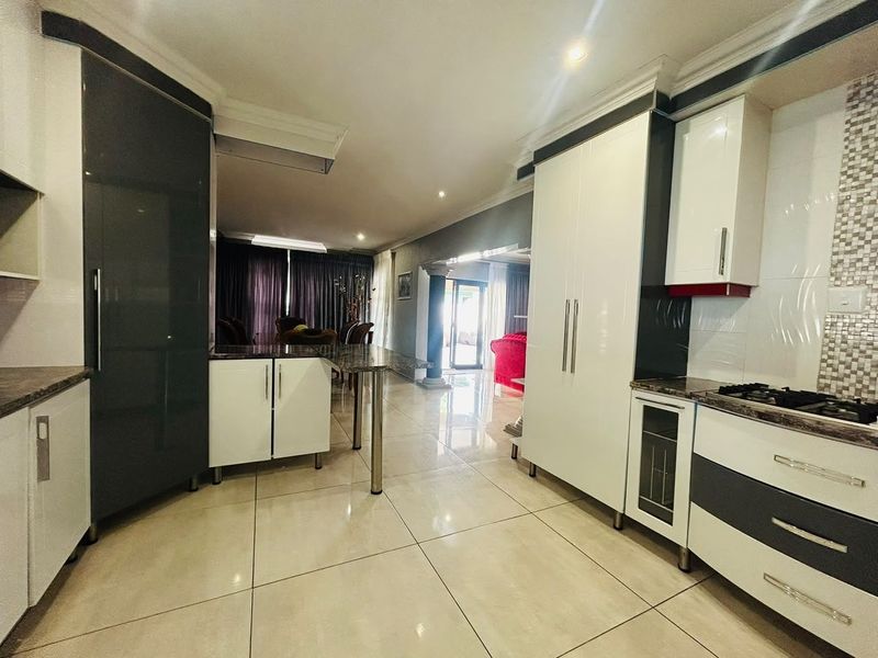 Modern open-plan kitchen featuring high-gloss cabinetry, granite countertops, and a gas hob, seamlessly flowing into the adjacent living and dining areas.