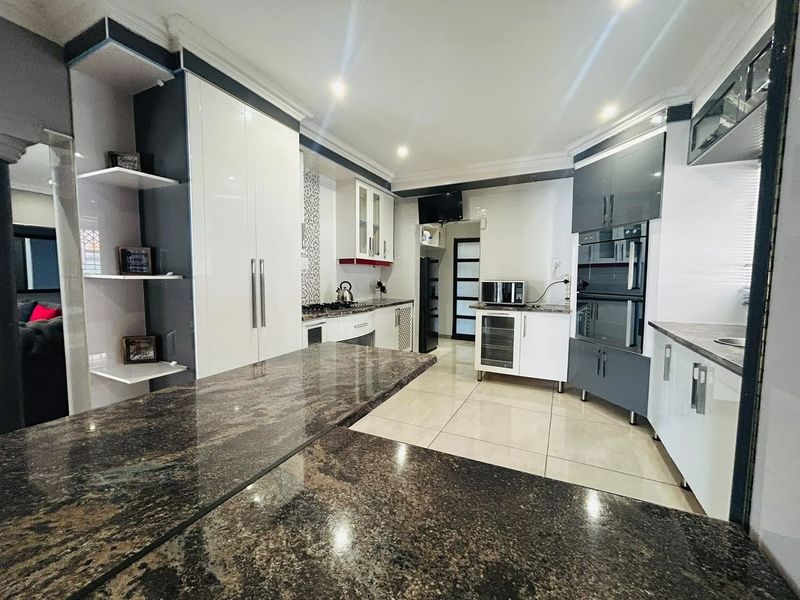 Modern kitchen featuring high-gloss cabinetry, granite countertops, built-in appliances, and tiled flooring with recessed lighting.