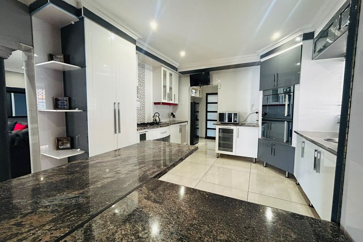Modern kitchen featuring high-gloss cabinetry, granite countertops, built-in appliances, and tiled flooring with recessed lighting.