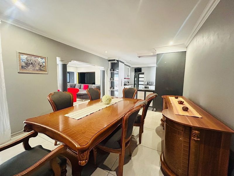 An open-plan dining area featuring tiled flooring, decorative columns, and crown molding, seamlessly flowing into the adjacent kitchen and living space.