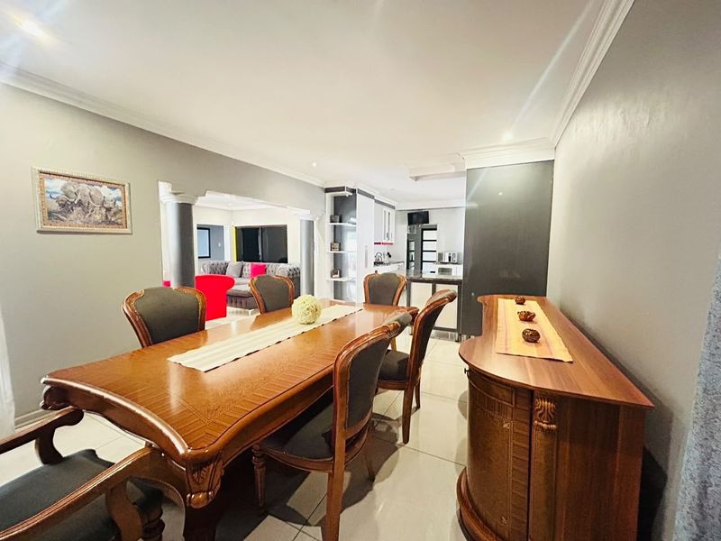 An open-plan dining area featuring tiled floors and crown molding, seamlessly flowing into a modern kitchen and adjacent living space.