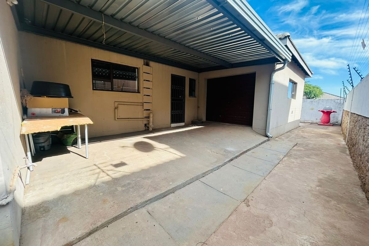 Rear exterior area featuring a covered patio space with concrete paving, a roller shutter garage door, and perimeter walling.